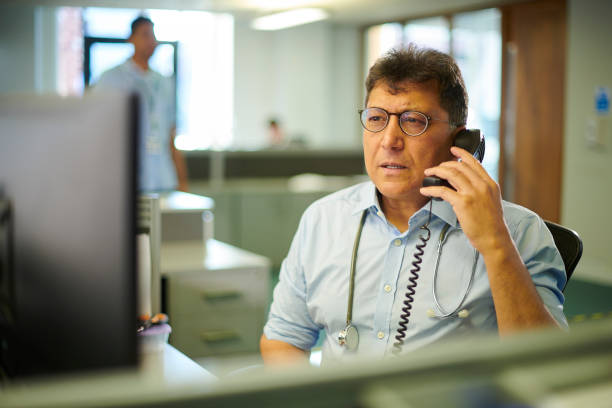 telephone triage mature doctor takes a triage telephone call triage stock pictures, royalty-free photos & images