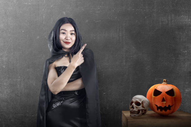 istock Asian witch woman with a cloak standing and showing with an empty space with a black wall background 1281427101