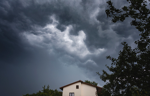 Dramatic stormy sky with rain wall behind and above roof of house with branches of tree on right.