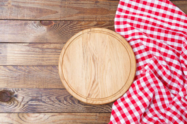 istock Brown old vintage wooden table with framed red checkered tablecloth and pizza cutting board.Thanksgiving day and Cristmas table concept. Top view and copy space. Selective focus 1281429378