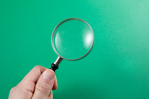 Human hand is holding magnifying glass on green background with copy space