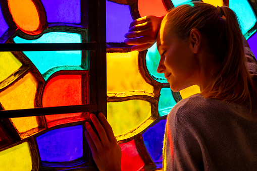 Nice Peaceful Female with Closed Eyes near the Colorful Stained Window Thinking about Future. Praying in the Church. Art and Religion Concept.