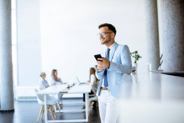 istock Happy young man using his mobile phone and smiling while his colleagues working in the background 1281434320