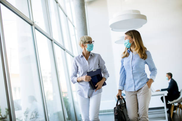 Businesswomen walking in the office and wearing mask as a virus protection Two businesswomen walking in the office and wearing mask as a virus protection briefcase photos stock pictures, royalty-free photos & images