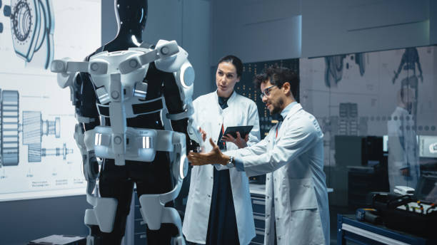 In Robotics Development Laboratory: Chief Female Engineer and Top Male Scientist Work on a Bionics Exoskeleton Prototype. Designing Powered Exosuit to Help Disabled People, Hard Labor Workers en el laboratorio de desarrollo de robótica: ingeniera jefe femenina y científica masculina superior trabajan en un prototipo de exoesqueleto biónico. diseño de exotraje accionado para ayudar a las personas discapacitadas, trabajadores trabajadores tra