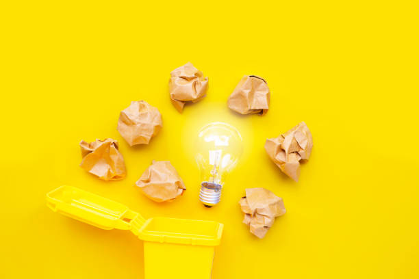 istock Yellow bin with light bulb and brown crumpled paper on yellow background. Ideas and creative thinking concept. 1281446711