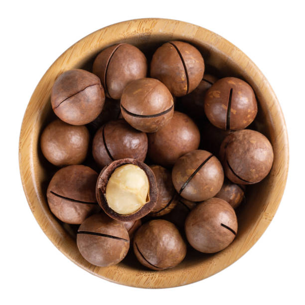 istock Macadamia nuts in wooden bowl isolated on white. Top view. 1281450731