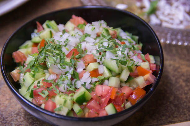 Fresh Israeli vegetables salad, containing cucumber, tomato white onion and parsley, served in a dark bowl stock photo