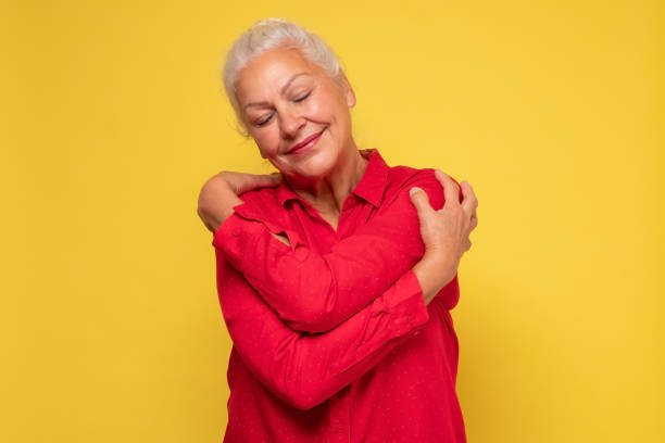 Woman wearing red clothes hugging herself being positive, smiling confident. Senior grey haired woman wearing red clothes hugging herself being positive, smiling confident. Self love and self care concept. hugging self stock pictures, royalty-free photos & images