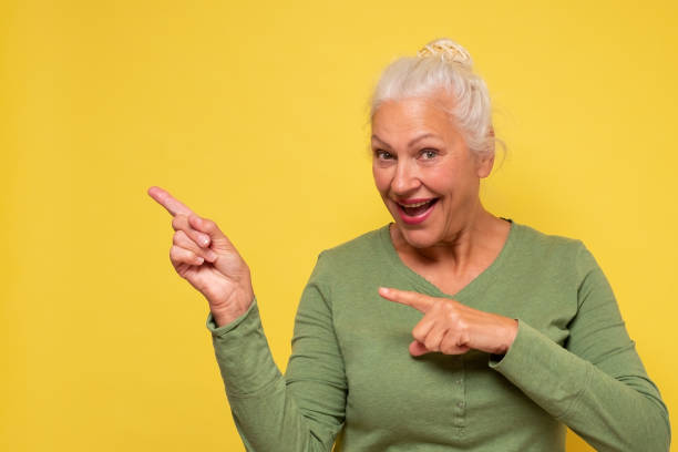 istock Senior woman pointing aside on copyspace. Studio shot on yellow wall. 1281456648