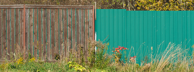 Photography of two different wooden fences in a Russian village. One is painted green, the other is unpainted. Neighbors concept. The topic of different income, lifestyle and social status.