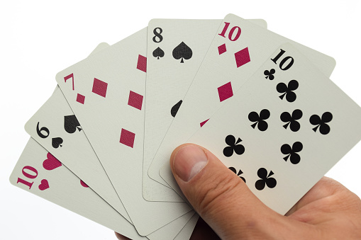 A man's hand holds a fan of six playing cards of different colors and suits. Photographed on a clean white background with clipping