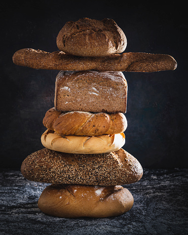 Bread baguette and bun stacked in column on dark backgropund