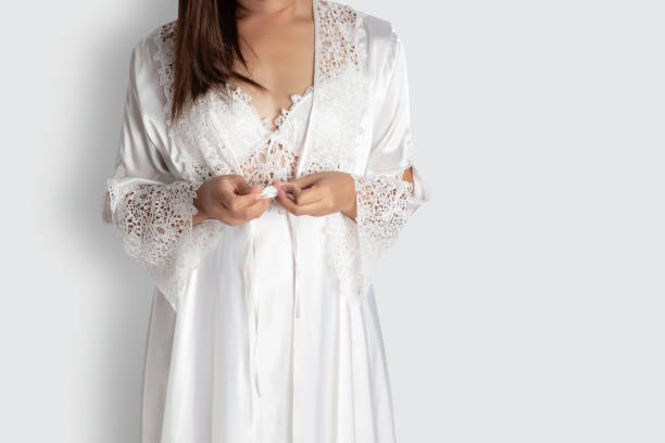 Women put on nightgown Women put on white sexy nightgown & long sleeve satin robe with floral lace, A girl trying on new white nightwear for sleep. Light gray empty space on right side Silky Nightwear stock pictures, royalty-free photos & images