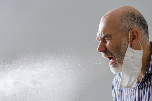 Man sneezing with spray of water droplet full of virus or microbes
He wears his face mask inappropriately on one ear