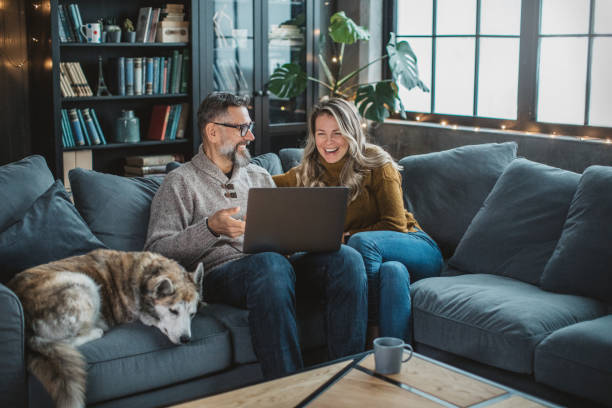 New normal way to hang with friends Mature couple at home using video call to talk with friends or family during pandemic isolation period. 55 59 years stock pictures, royalty-free photos & images