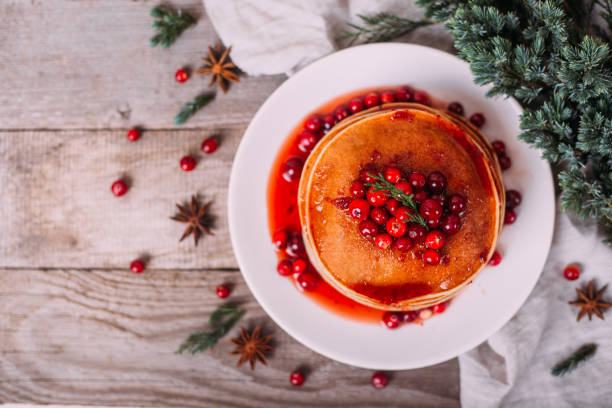 istock Stack of american pancakes with fresh cranberry and jam in white plate on wooden rustic table decorated Christmas tree, delicious dessert for breakfast in winter, vintage style. Copy space. 1281475742