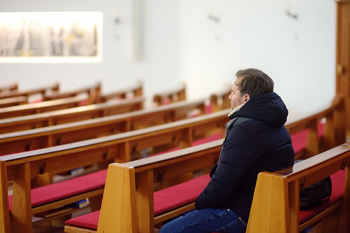 Religious middle age man praying in catholic church. Person closing his eyes, begging for forgiveness and blessing from God. Catholicism is Christianity religion.