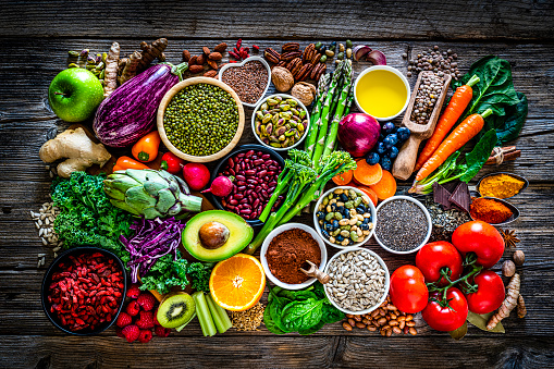 Vegan food backgrounds: top view of a wooden table filled with fresh organic fruits, vegetables, seeds and nuts. This type of food is rich in antioxidants, flavonoids, fiber, vitamins and minerals recommended in a well balanced vegan diet. The composition includes artichoke, eggplant, avocado, kale, tomato, spinach, celery, broccoli, asparagus, onion, carrot, garlic, sweet potato, radish, ginger, turmeric, pepper, kidney bean, soy bean, kiwi, apple, orange, blueberry, raspberry, goji berry, chia seed, sunflower seed, pistachio, flax seed, cocoa powder, dark chocolate, brown lentil, almond, pecan, walnut, among others. High resolution 42Mp studio digital capture taken with SONY A7rII and Zeiss Batis 40mm F2.0 CF lens