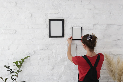 Woman arranging picture frames on wall in new house, diy home improvement concept