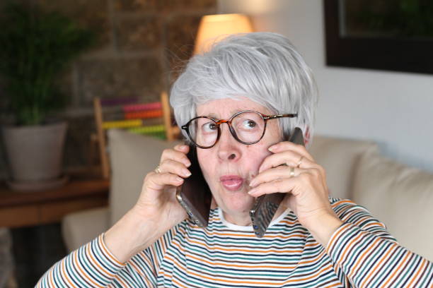 istock Senior overwhelmed woman using two cellphones 1281479940