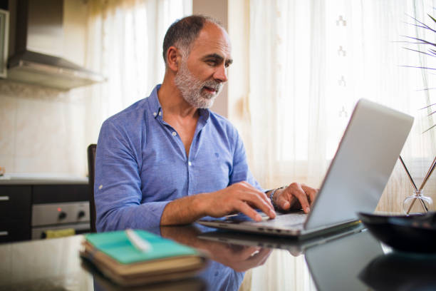 istock Smiling mature man using a laptop and working from home 1281483459