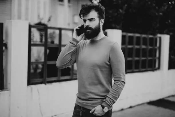 Photo of Young bearded man walking in the city street and talking on the phone