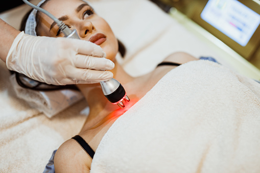 Young woman lying down in the beauty clinic and having an ultrasound cavitation treatment to lift the skin and remove body fat
