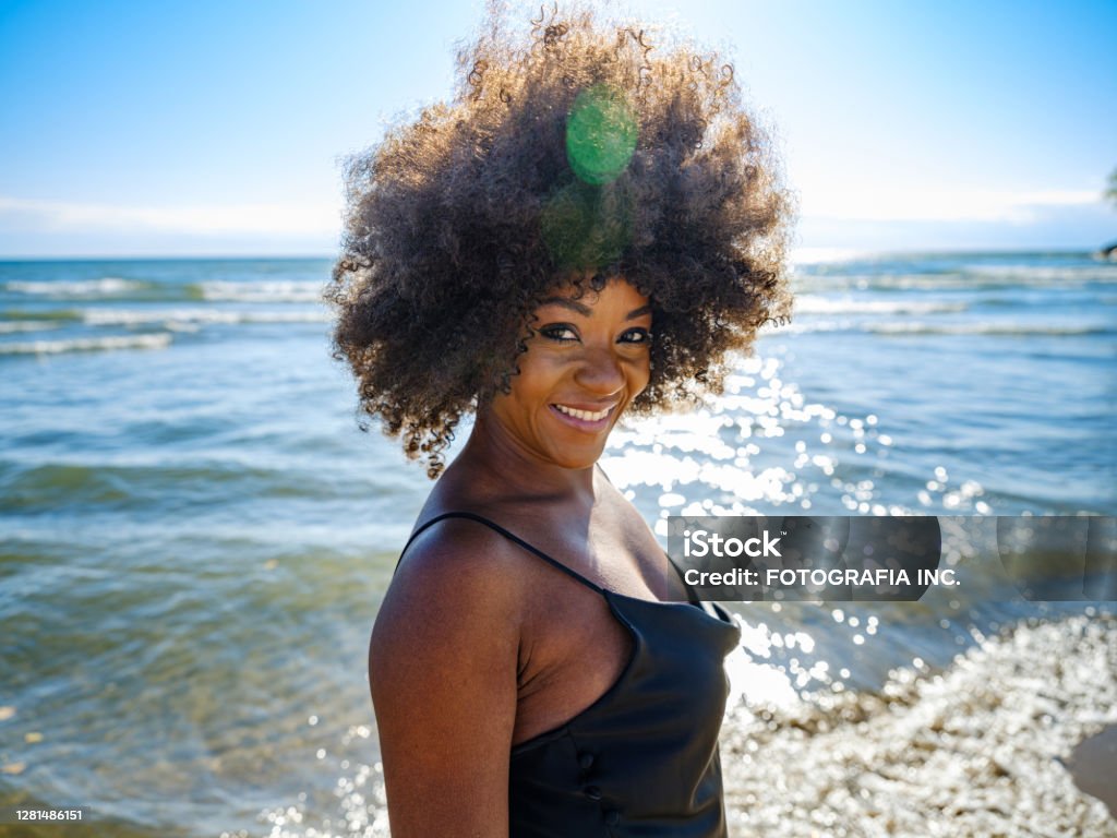 African woman on a sandy beach Young African woman wearing black dress, relaxing on the sandy beach. Sunny day in October. Black Color Stock Photo