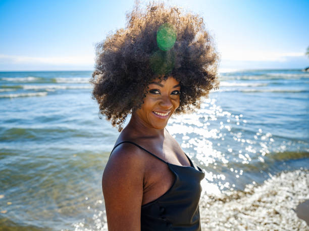 African woman on a sandy beach Young African woman wearing black dress, relaxing on the sandy beach. Sunny day in October. cheesy grin photos stock pictures, royalty-free photos & images