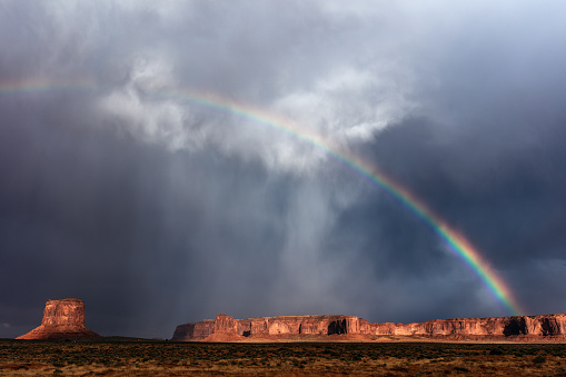 Scenic landscape view of Monument Valley with a rainbow and stormy sky.