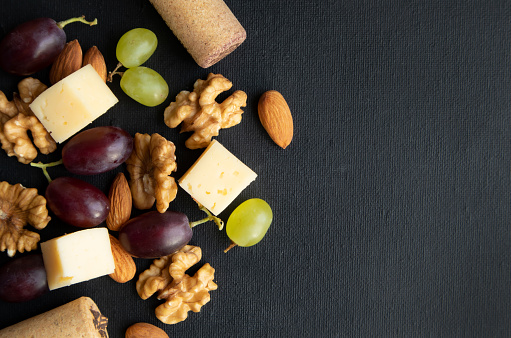 Maasdam cheese. walnut and berries of purple and green grapes on a dark background with space for text.