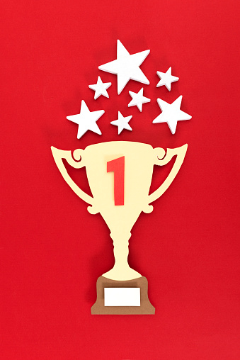 Yellow trophy made of paper with number 1 in red on it on red background with stars over it.