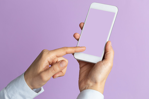 Unrecognizable person is showing screen of smart phone to camera and is pointing with one finger at device screen in front of purple background.
