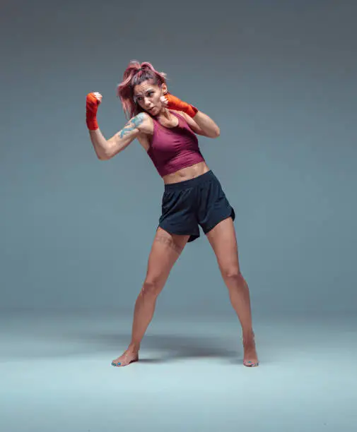 Photo of Female fighter trains in boxing bandages in studio on gray background.