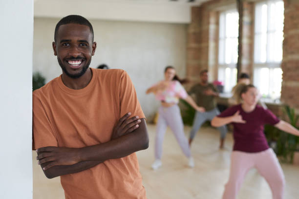 African dance instructor Portrait of African young man working as a dance instructor smiling at camera with people exercising in the background dance studio instructor stock pictures, royalty-free photos & images