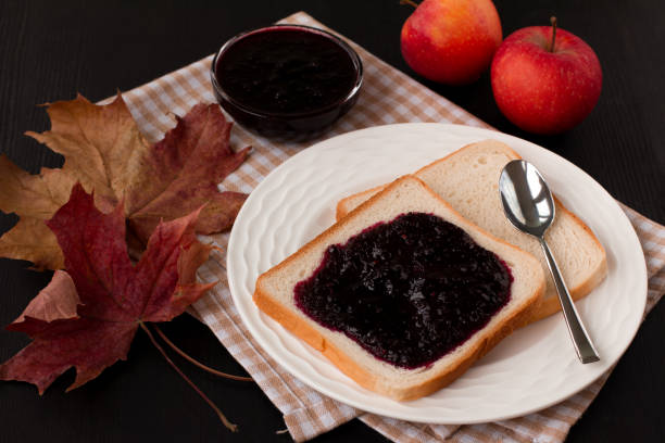 istock Black currant jam on fresh bread. Black table, maple leaves and red apples. The idea of Breakfast and good mood 1281495799
