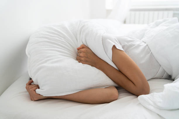 枕を覆うベッドの上に一人で横たわっているうつ病の女性は、不眠症、隣人の大きな音に苦しんで、彼女の夫と離婚した後、精神的な問題を抱えています - relationship difficulties audio ストックフォトと画像