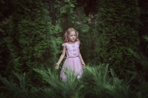 Sweet girl in a pink dress standing in the fairy forest.