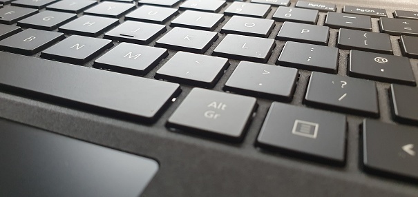 Close up of a dark grey computer keyboard on a desk with external day light.  This picture was taken in London 2020