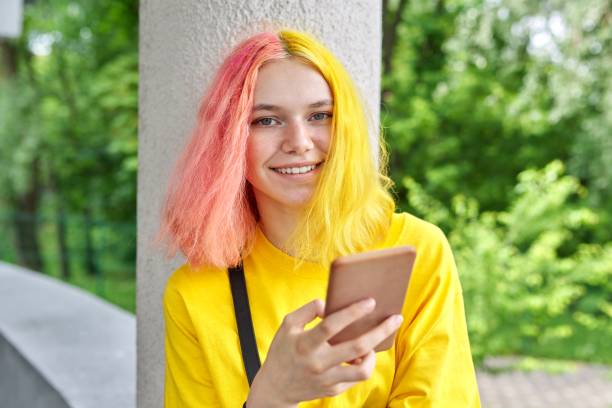 Fashionable teenager girl with colored dyed hair with a smartphone outdoors. Fashionable teenager girl with colored dyed hair with a smartphone outdoors. Smiling bright young woman in yellow t-shirt with yellow pink hair pink hair stock pictures, royalty-free photos & images