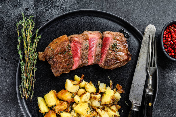 bistecca di striploin alla griglia con patate, carne di manzo. sfondo nero. vista dall'alto - steak strip steak prepared potato grilled foto e immagini stock