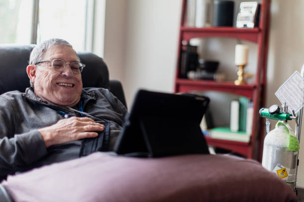 Senior man relaxing and having a good time while sitting in a recliner and watching funny content on his tablet. Real life photography oxygen cylinder stock pictures, royalty-free photos & images