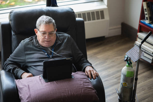 Senior man relaxing and having a good time while sitting in a recliner and watching funny content on his tablet. Real life photography oxygen tank stock pictures, royalty-free photos & images
