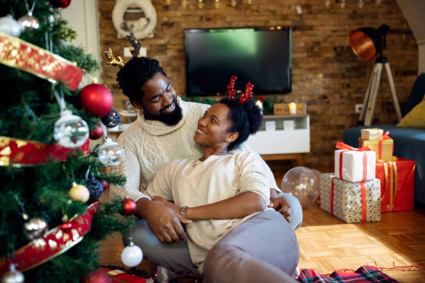 istock Happy black couple talking while relaxing by Christmas tree at home. 1281508574