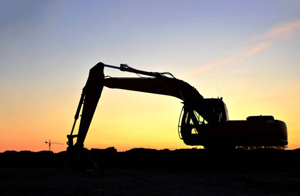 istock Silhouette of the heavy tracked excavator at a construction site on a background sunset. 1281509200