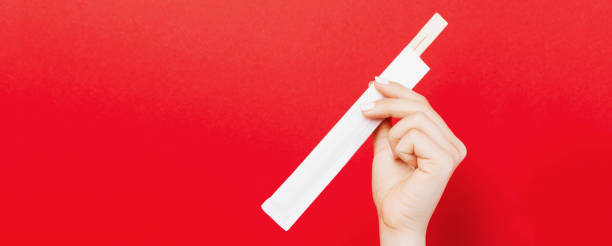 istock Woman's hand holding chopsticks in a pack on red background. Chinese food concept with empty space for your design 1281515616