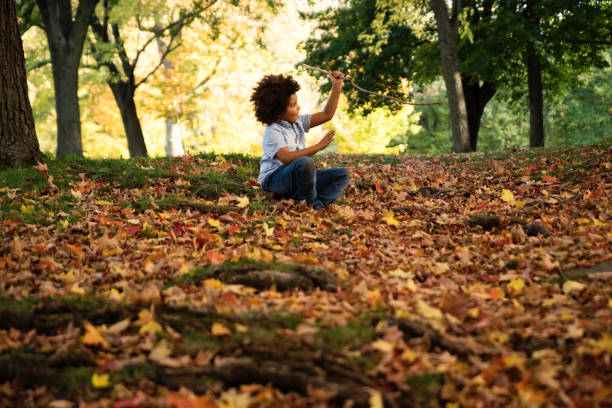 A boy rolls upside down while playing on yellow autumn leaves in the garden.