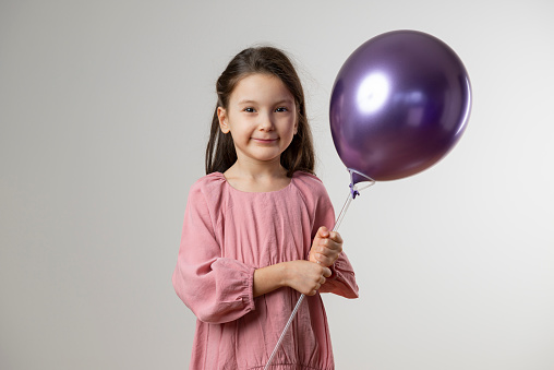 Girl is looking at camera and holding purple balloon.