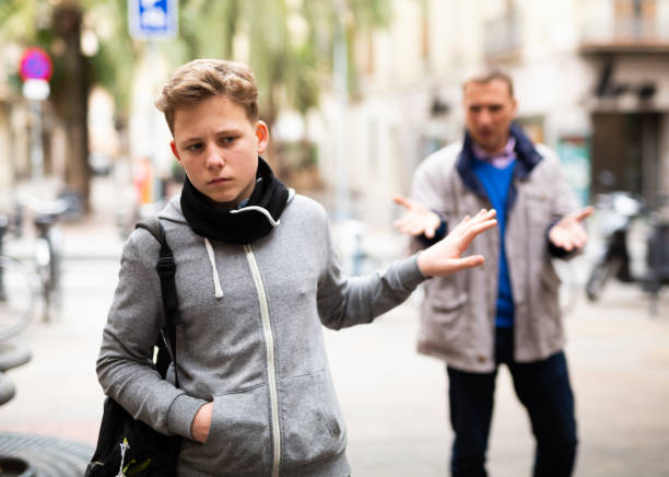 Frowning teenager gesturing enough while man reprimanding him